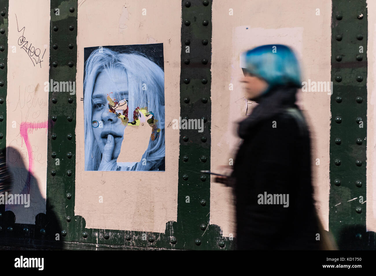 Femme floue avec des cheveux bleus en passant devant un mur avec le street art photographie murale portrait de jeune enfant à Brick Lane, Shoreditch, East London, UK Banque D'Images