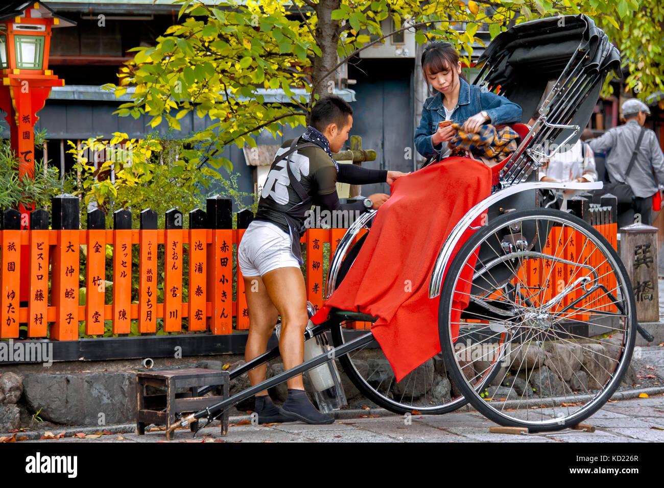 Rue Shirakawa de Gion, Kyoto, Japon - 23 octobre 2016 : conducteur de pousse-pousse assure une couverture rouge à son client alors qu'elle s'installe pour son chemin. Banque D'Images