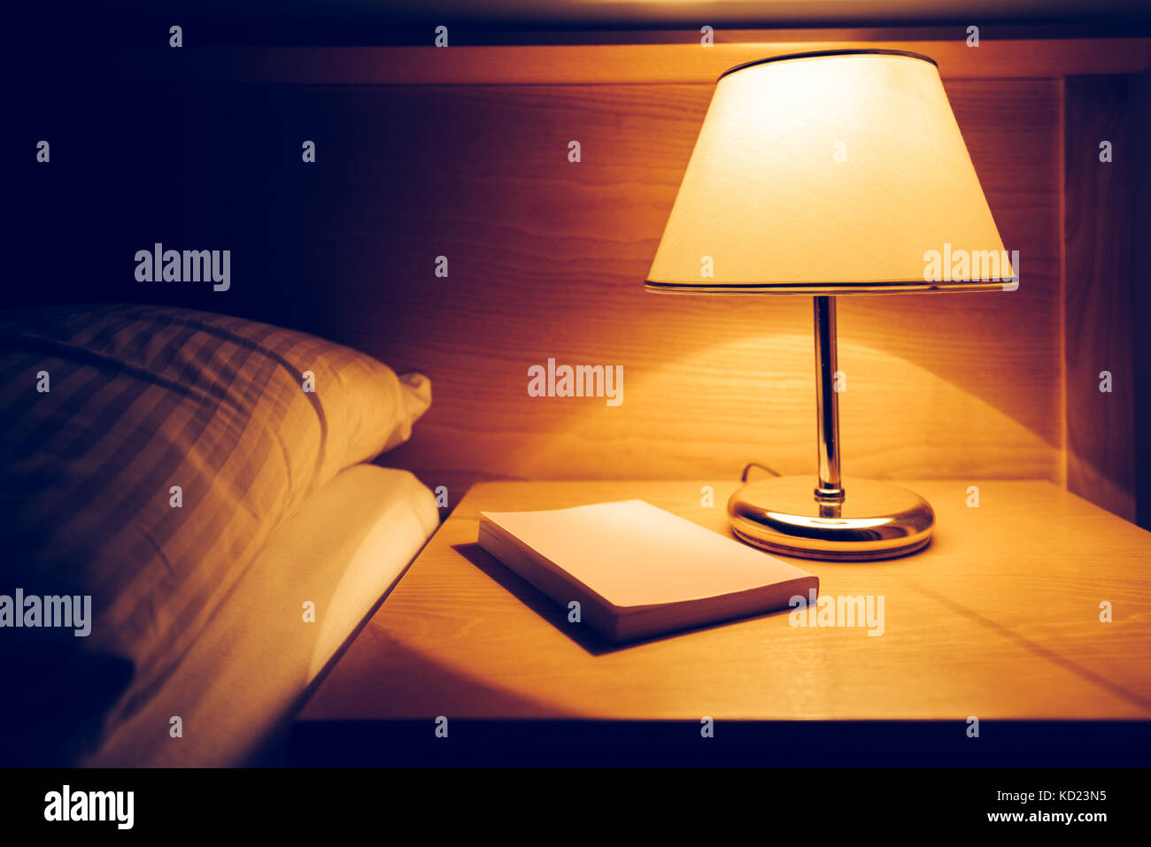 Réservez et lampe sur table de nuit dans la chambre d'hôtel à côté du lit vide et l'oreiller Banque D'Images