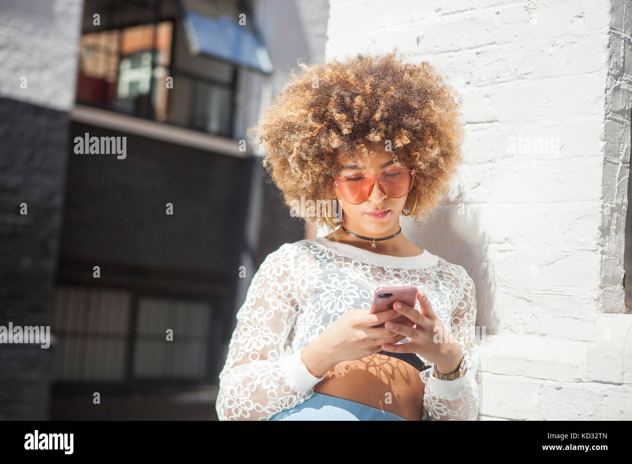 Jeune femme à l'extérieur, leaning against wall, looking at smartphone Banque D'Images