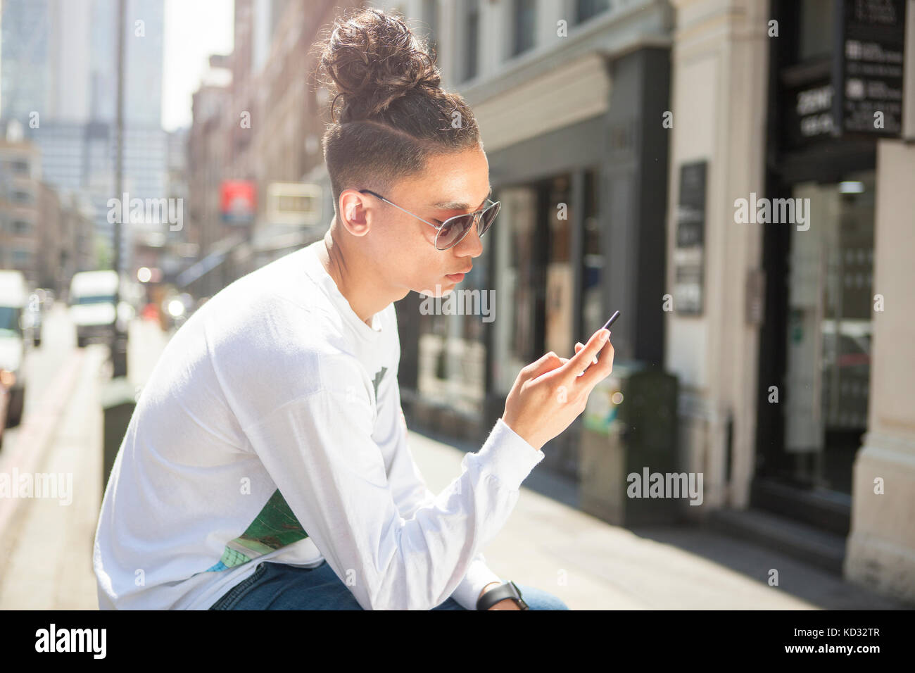 Jeune homme assis à l'extérieur, using smartphone Banque D'Images