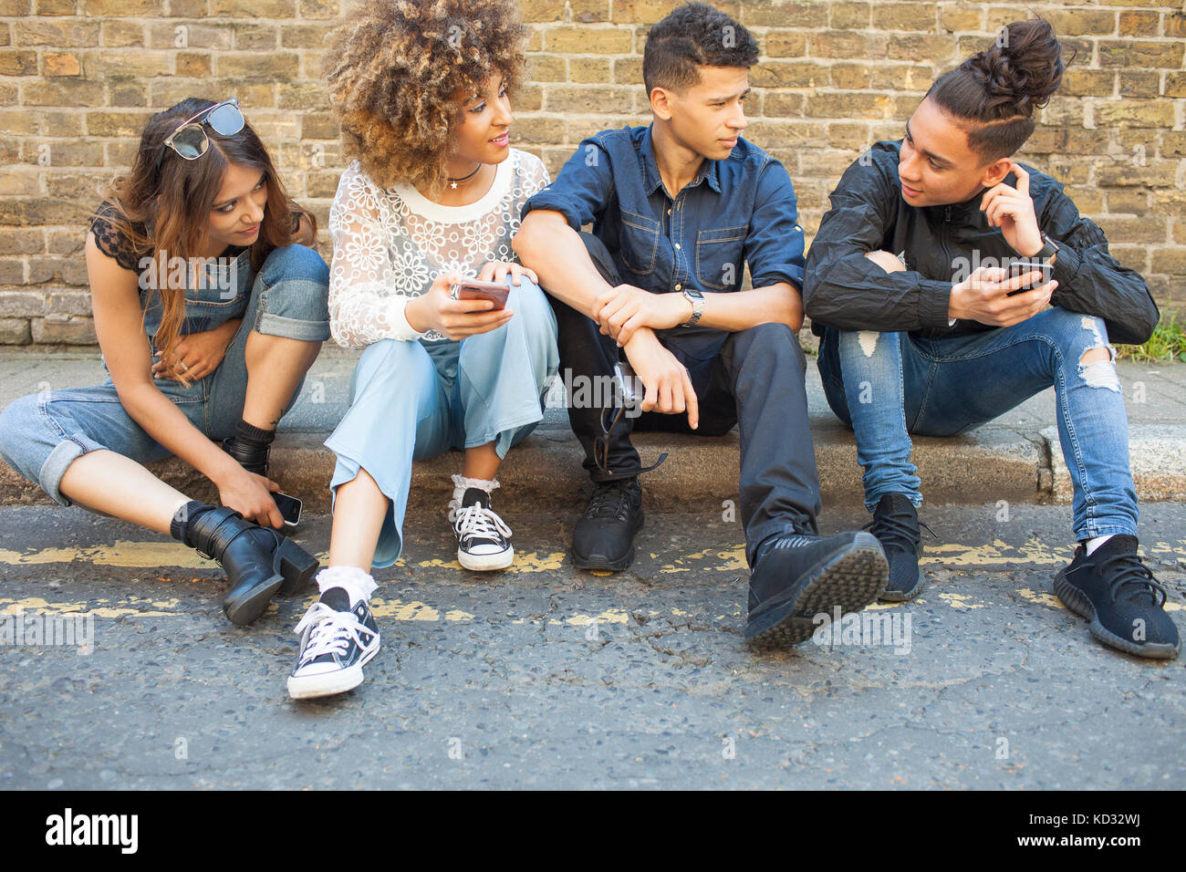 Quatre amis assis dans street, à la recherche de téléphones intelligents Banque D'Images