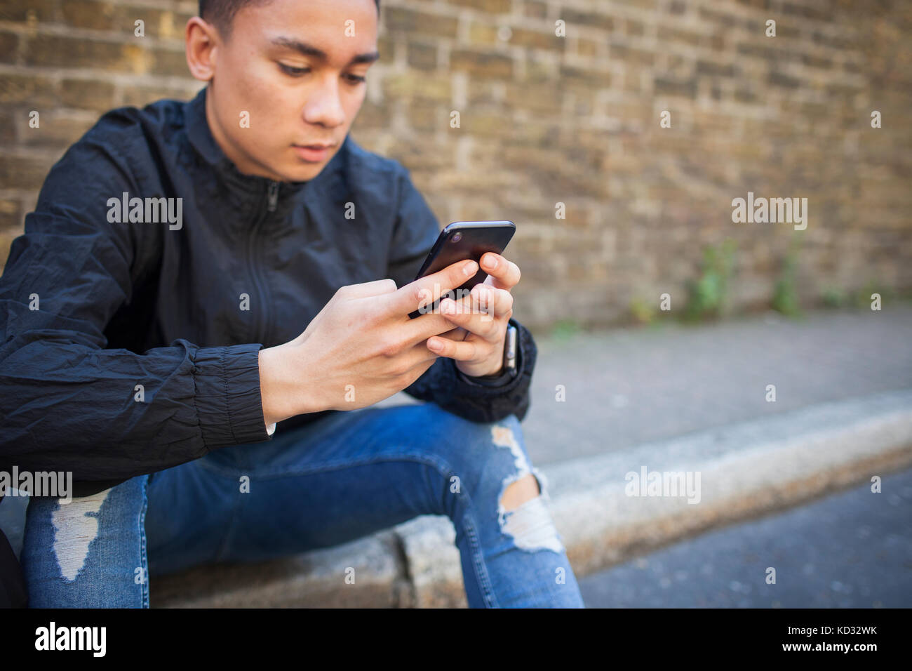 Jeune homme assis à l'extérieur, using smartphone Banque D'Images