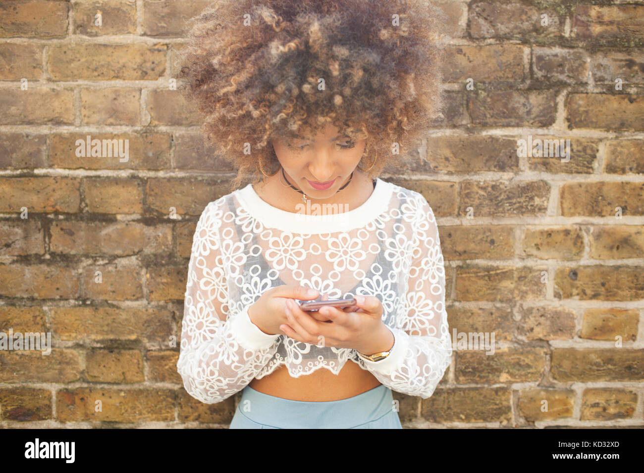 Young woman leaning against wall, using smartphone Banque D'Images