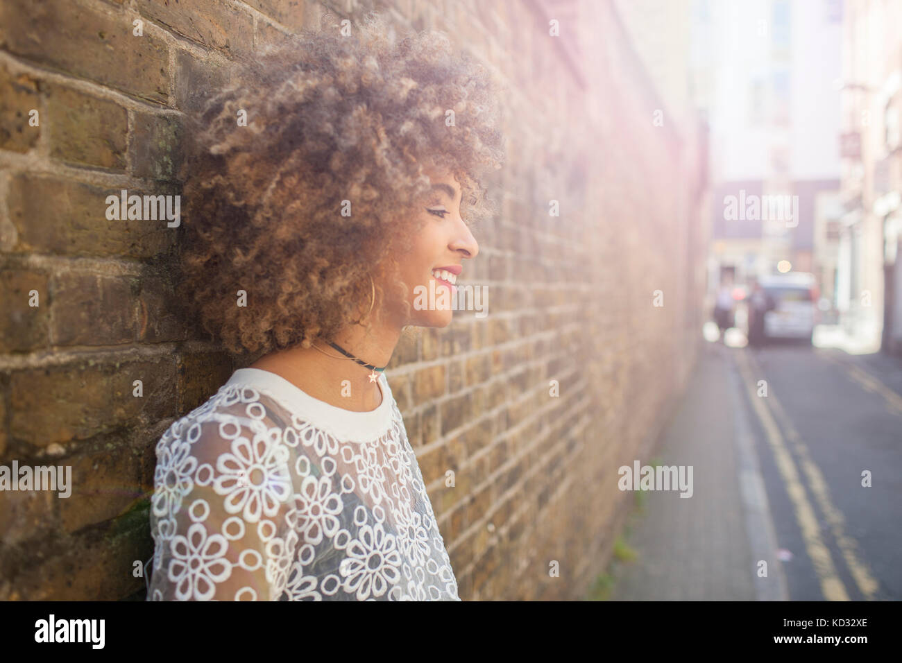 Young woman leaning against wall, smiling Banque D'Images