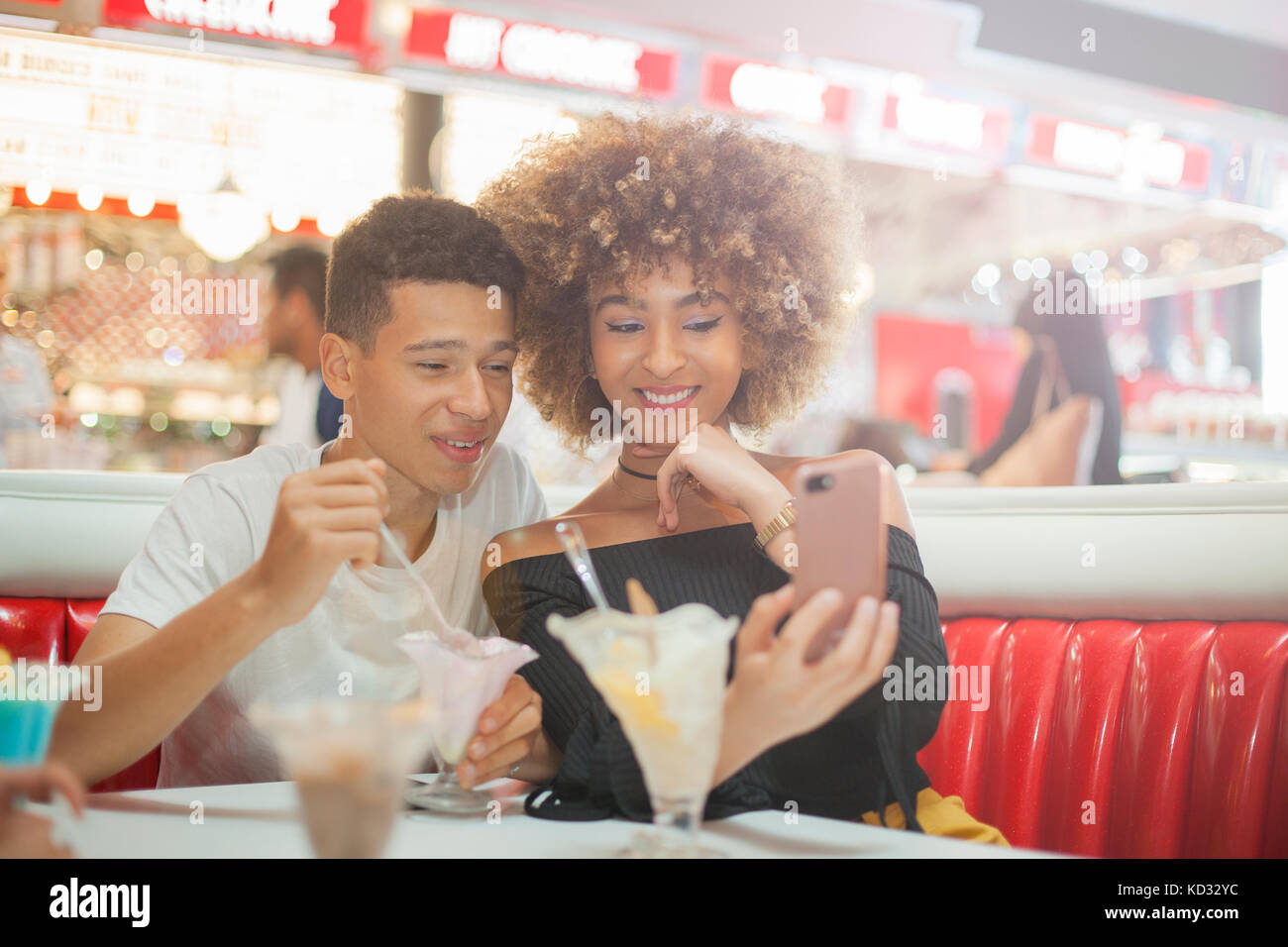 Young couple sitting in diner, looking at smartphone, rire Banque D'Images