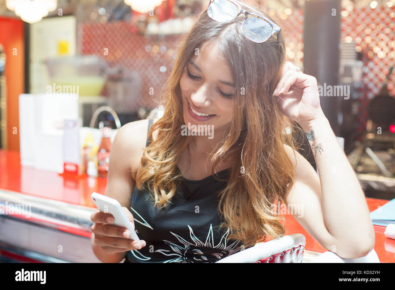 Young woman sitting in cafe, looking at smartphone, smiling Banque D'Images