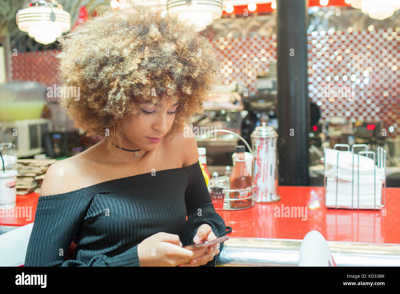 Jeune femme assise au diner, looking at smartphone Banque D'Images