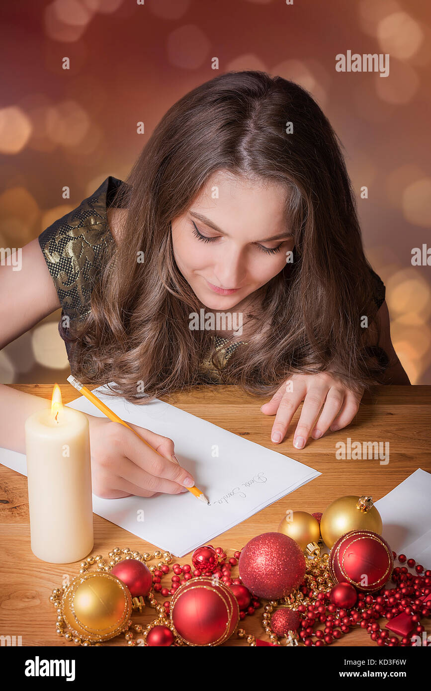Belle jeune fille écrit au père Noël, aux chandelles, entouré de globes colorés et d'autres décorations de Noël. Banque D'Images