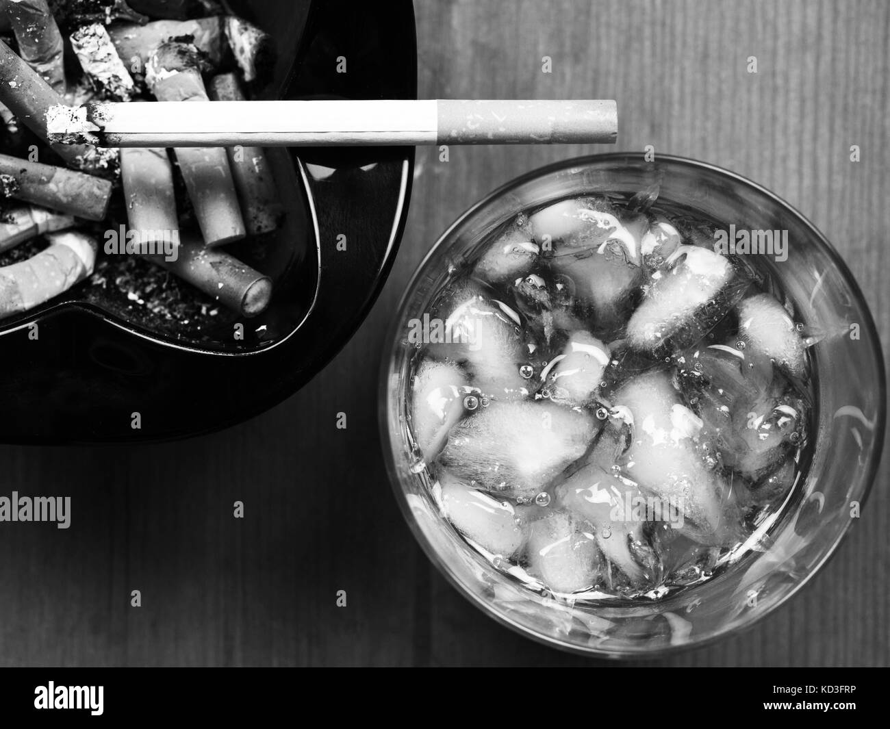 Imaqge monochrome noir et blanc d'un verre de whisky écossais et d'une cigarette allumée sur un cendrier Banque D'Images