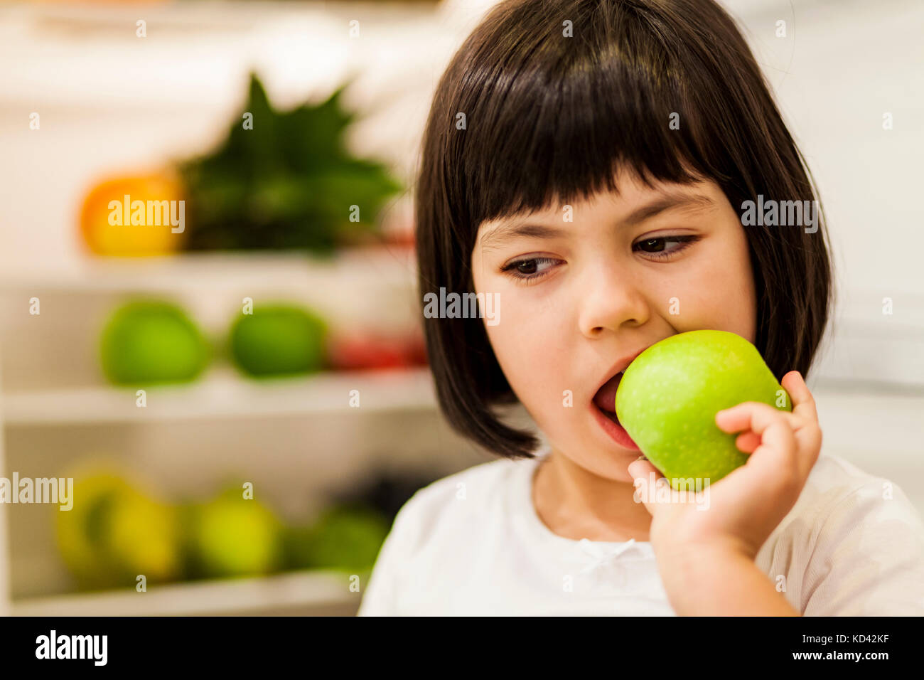 Portrait of cute black hair little girl eating apple Banque D'Images