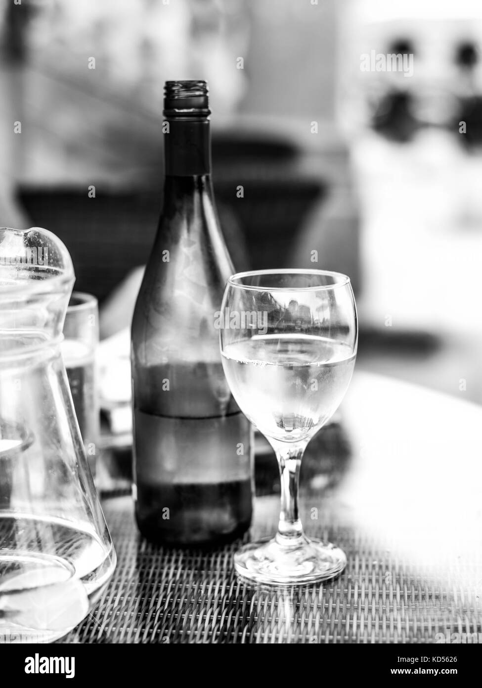L'image monochrome noir et blanc d'un verre de vin blanc à côté d'une bouteille de vin sur une table avec une carafe d'eau Banque D'Images