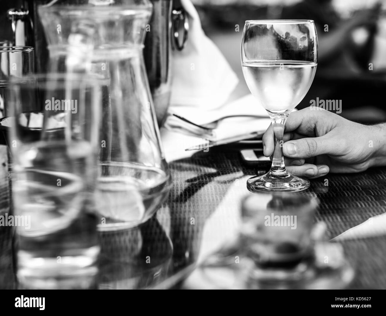 L'image monochrome noir et blanc d'un homme tenant un verre de vin blanc avec une cruche d'eau sur une table mise Banque D'Images