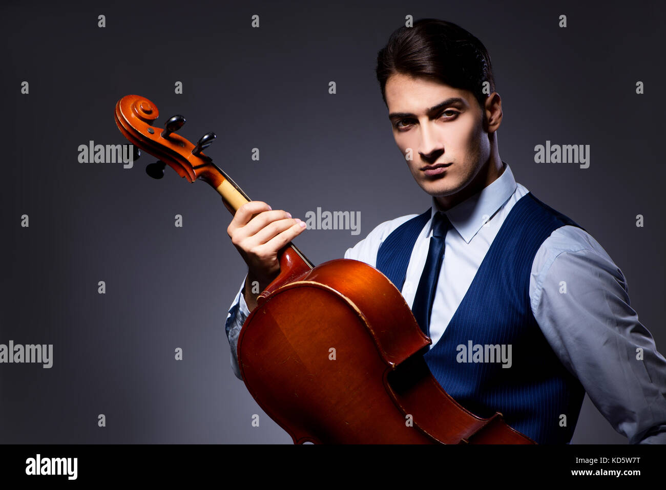 Jeune homme jouant du violoncelle in dark room Banque D'Images