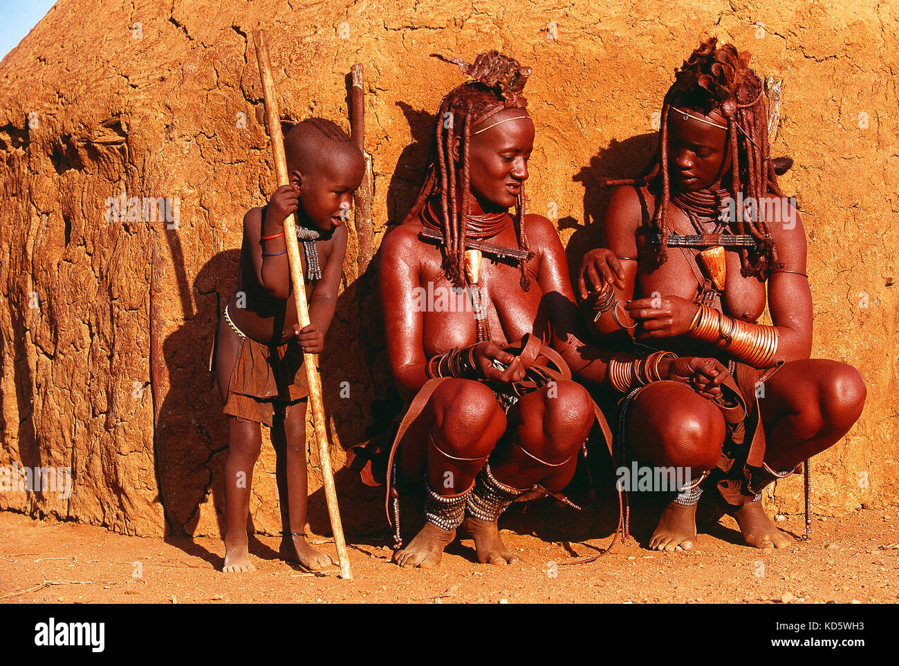 Namibie. Région de Kunene. Deux femmes Himba et un enfant près d'une hutte de boue. Banque D'Images