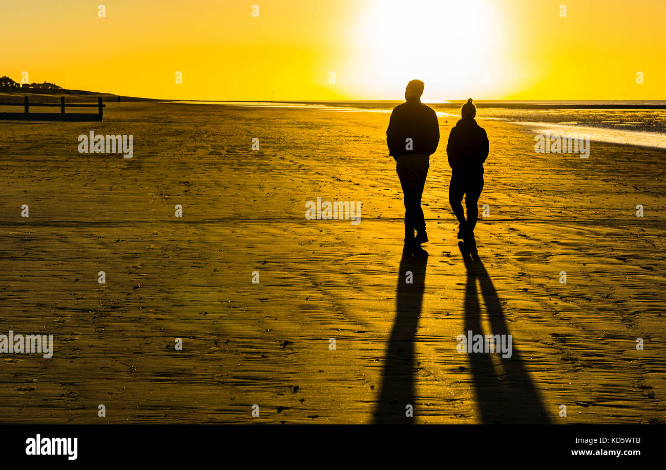 Silhouette d'un couple en train de marcher sur une plage de sable fin très tôt le matin avec de longues ombres au lever du soleil, au Royaume-Uni. Banque D'Images