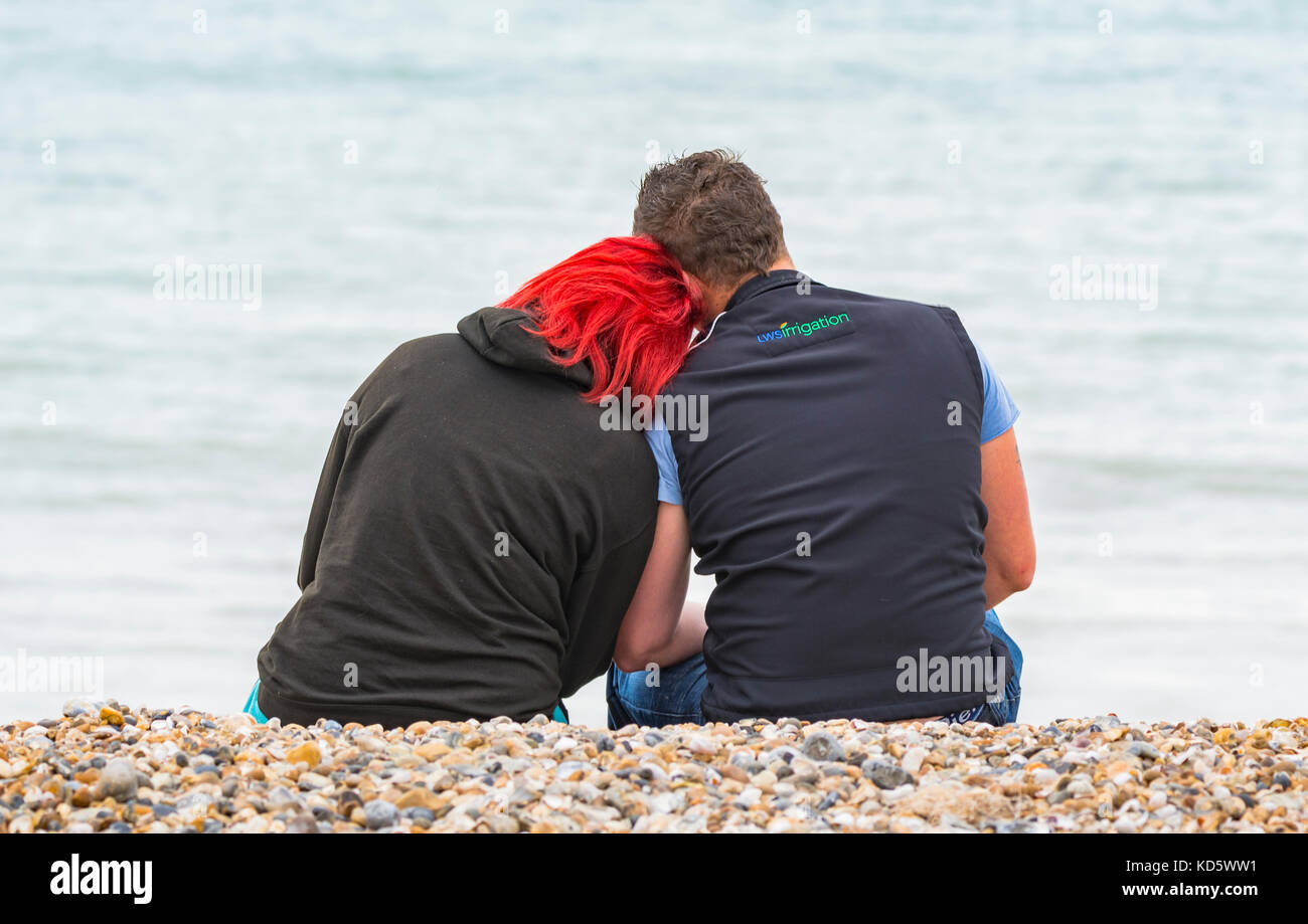 Jeune couple assis sur une plage au bord de la mer le partage d'un moment. Banque D'Images