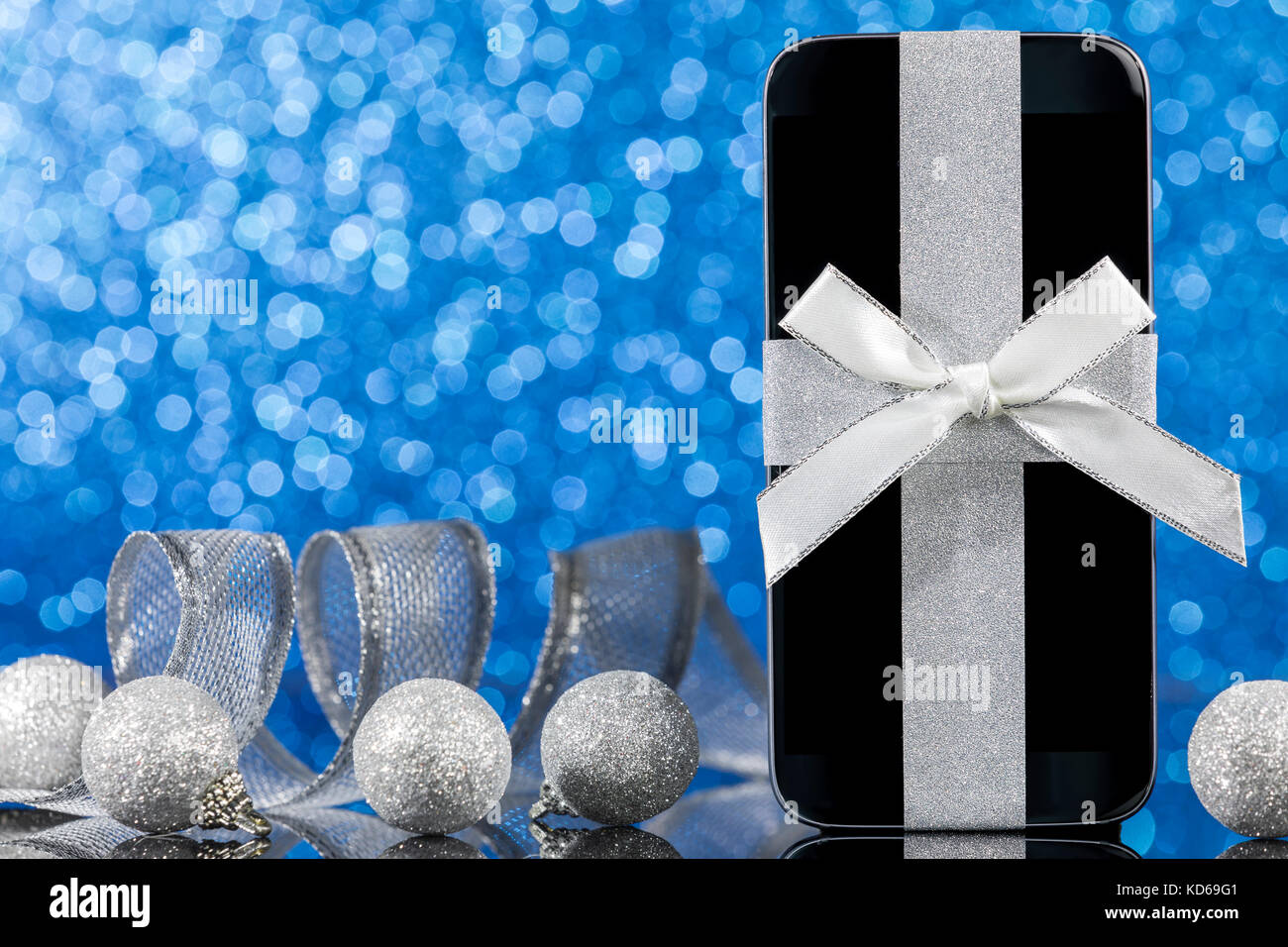 Smartphone et décorations pour arbre de Noël sur la table en verre noir sur fond bleu. L'accent sur smartphone. Banque D'Images