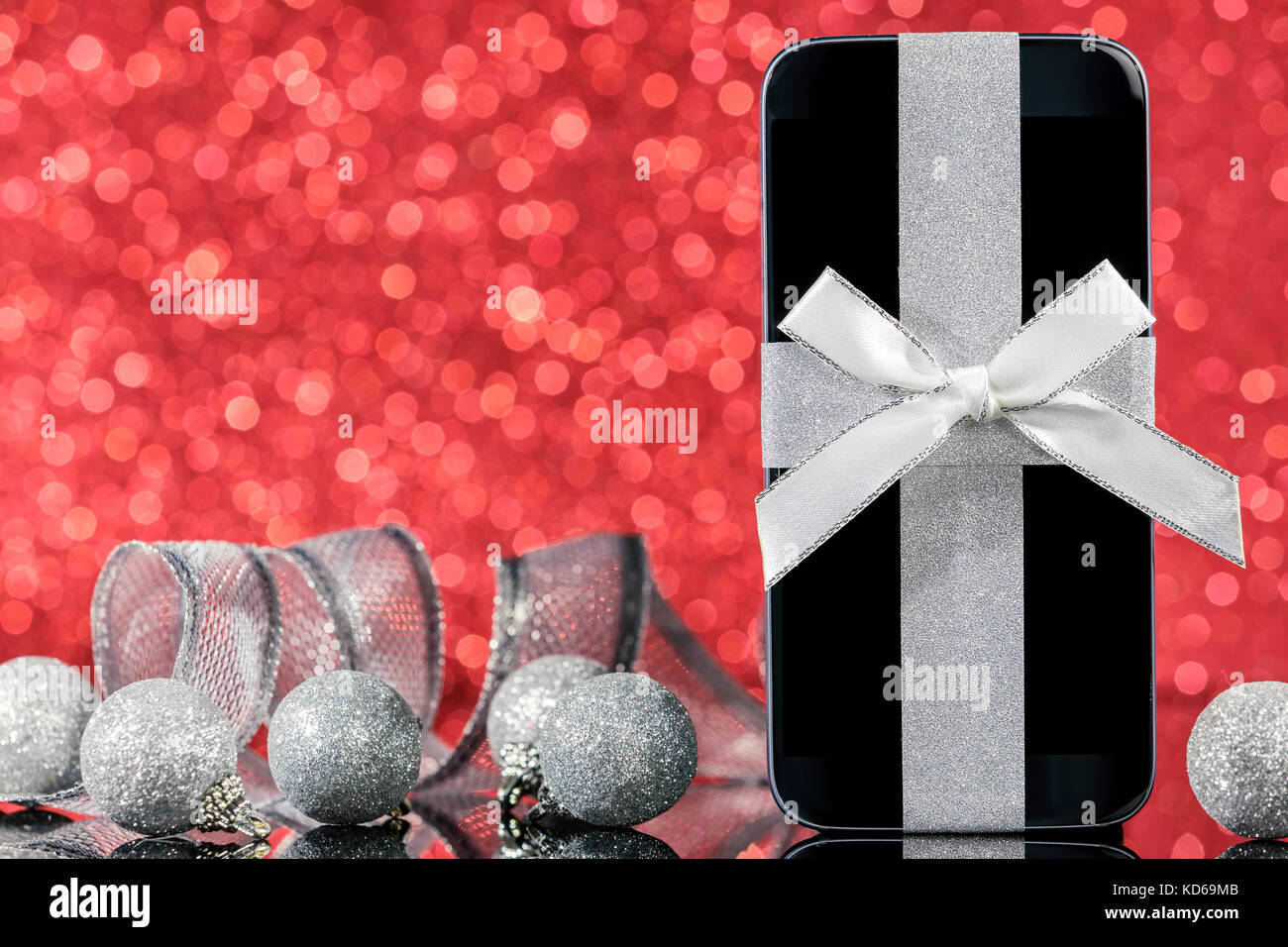 Smartphone et décorations pour arbre de Noël sur la table en verre noir sur fond rouge. L'accent sur smartphone. Banque D'Images