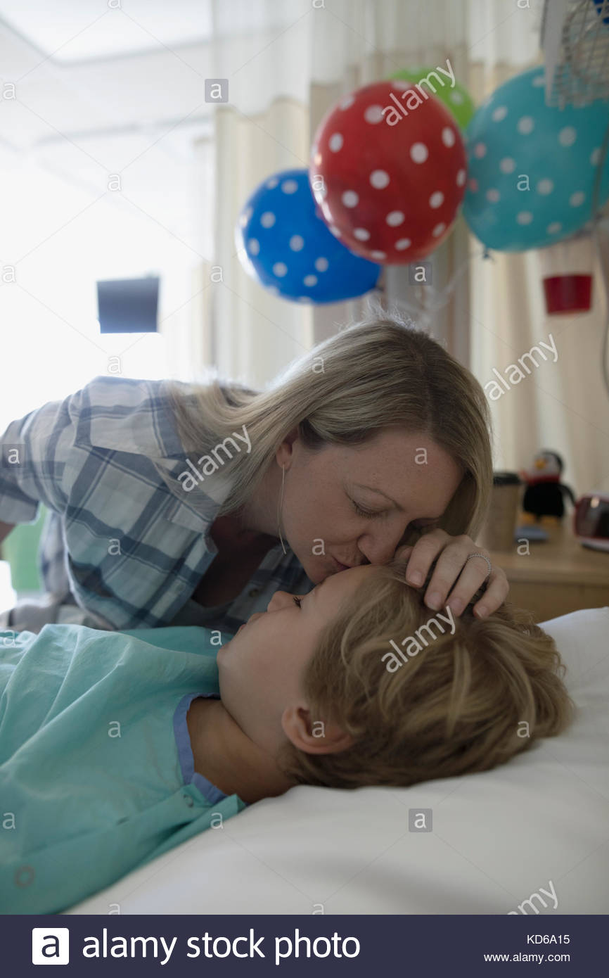 Une mère affectueuse embrasse le front de son garçon endormi patient dormant dans le lit d'hôpital Banque D'Images