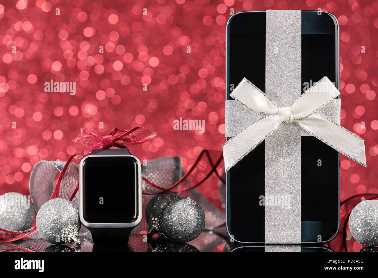 Smartphone et smartwatch et décorations pour arbre de Noël sur la table en verre noir sur fond rouge. L'accent sur smartphone. Banque D'Images