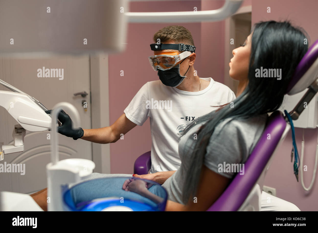 Jeune femme est examiné par un médecin en cabinet dentaire. male dentist dans des gants, lunettes et masque de protection examine l'ordinateur dans l'unité dentaire. Banque D'Images