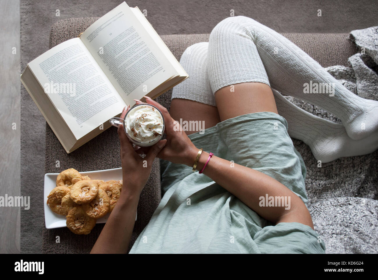 Pretty girl reading book à la maison sur la table avec du lait au chocolat chaud et cookies Banque D'Images