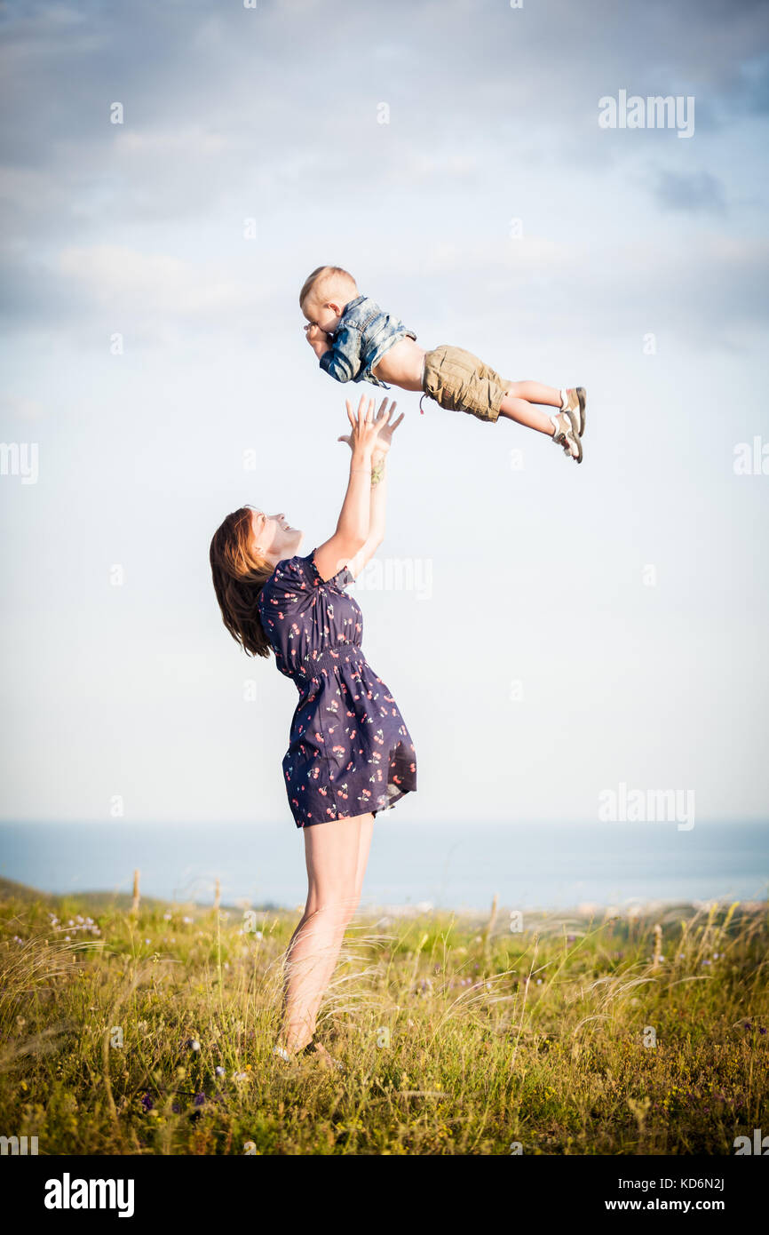 Maman soulève un enfant dans ses bras contre le ciel Banque D'Images