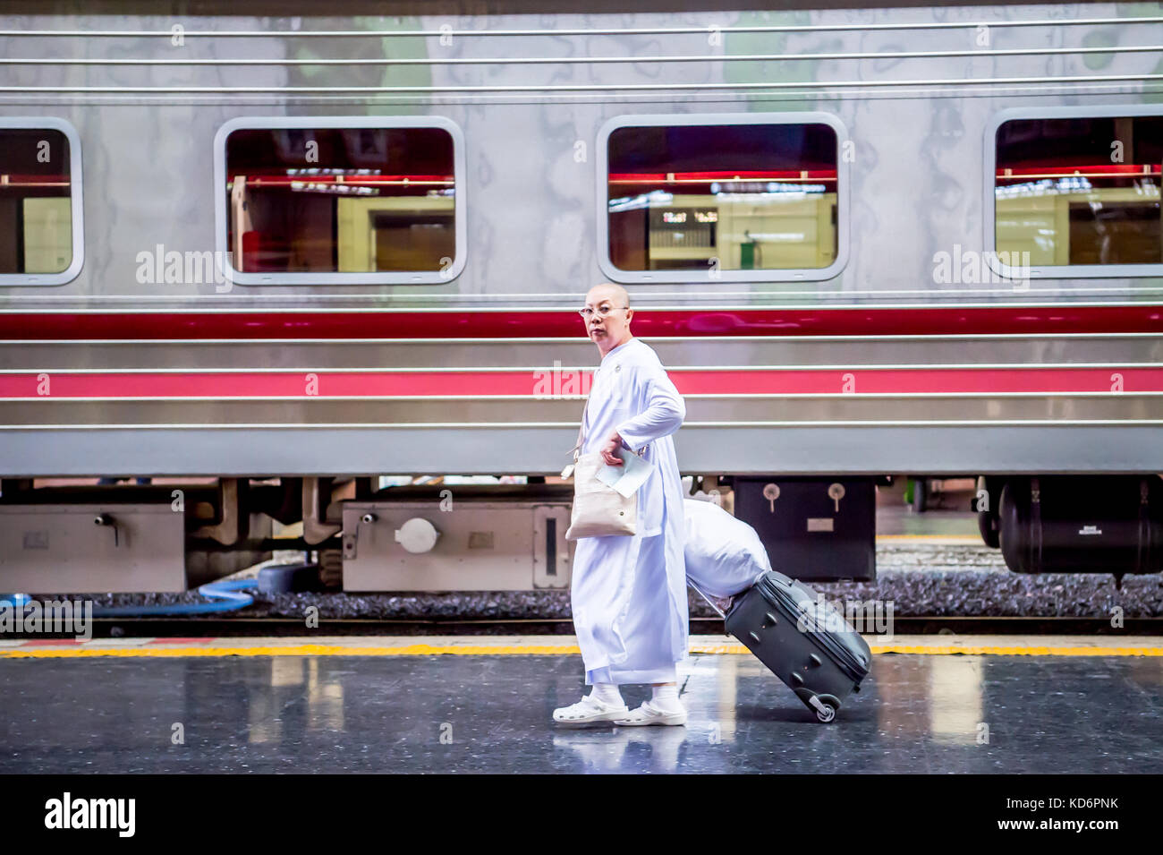 Une nonne bouddhiste thaï fait son chemin à travers la plate-forme du train transportant des bagages à la gare de hua lamphong dans le centre de Bangkok en Thaïlande en Asie. Banque D'Images