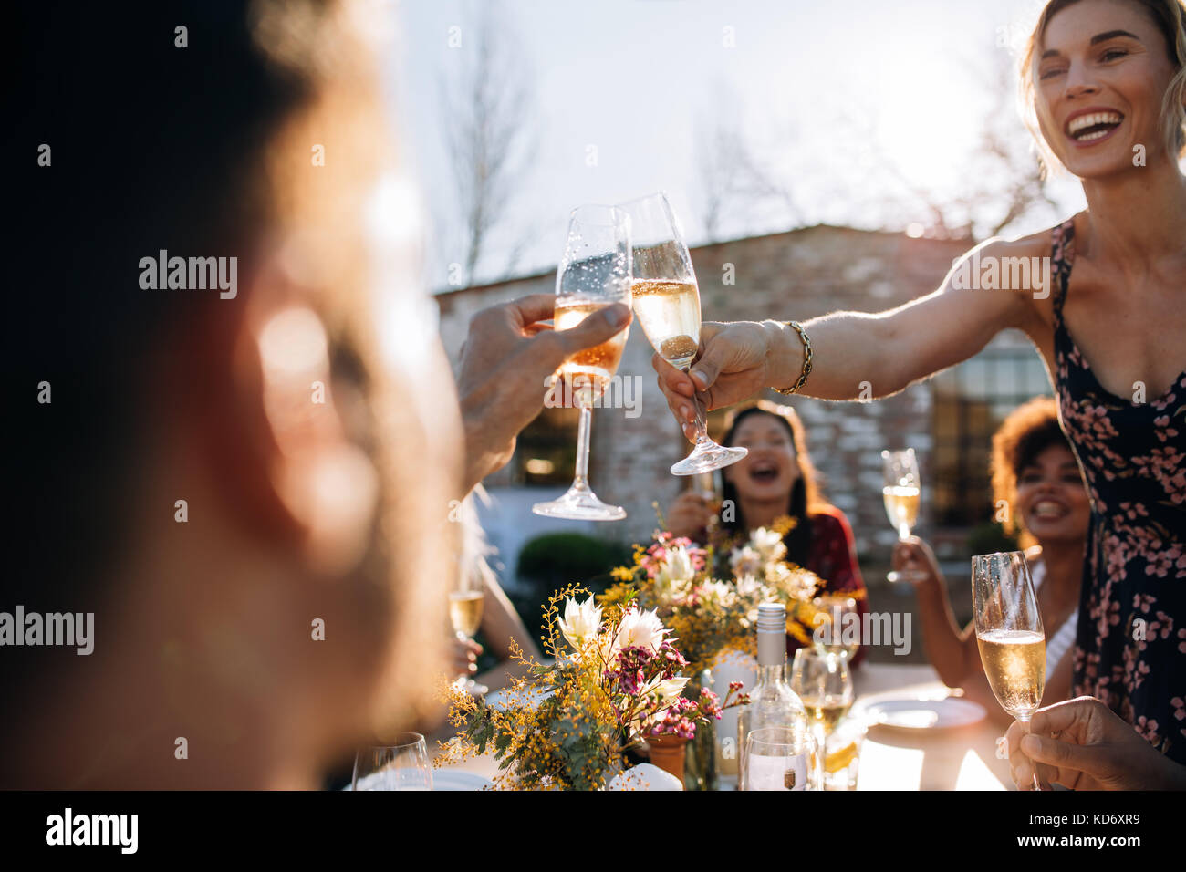 Smiling young woman toasting champagne avec ami pendant une fête en plein air. Les jeunes bénéficiant de party avec accent sur les verres de champagne. Banque D'Images