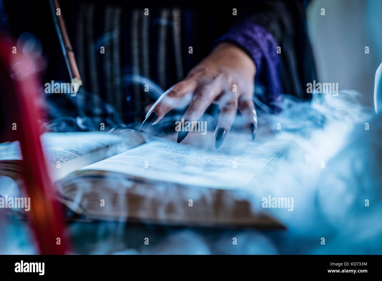 Close-up of a witch's part avec des clous noir fumé sur livre de recette magique et avec une baguette magique. Banque D'Images