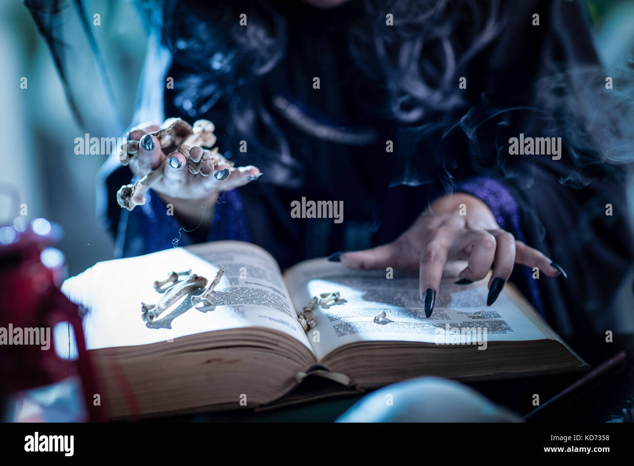 Close up of a witch's mains avec ongles tenant noir souligné ci-dessus les os d'un livre de recette magique. Banque D'Images