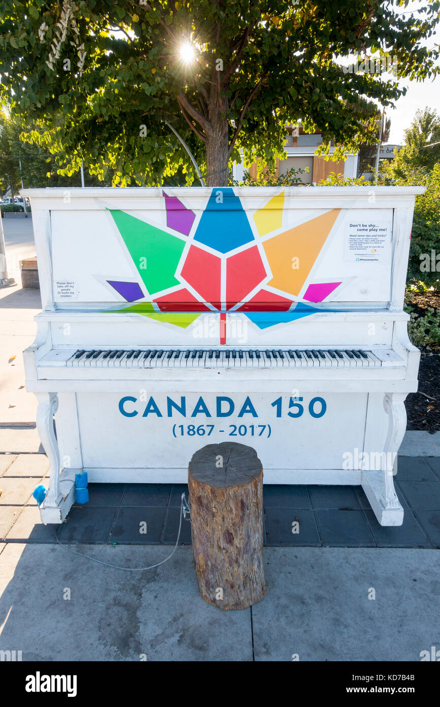Piano placé dans Kelowna's Waterfront Park pour le 150e anniversaire du Canada. Un panneau invite toute personne passant par d'arrêter et de jouer. Banque D'Images