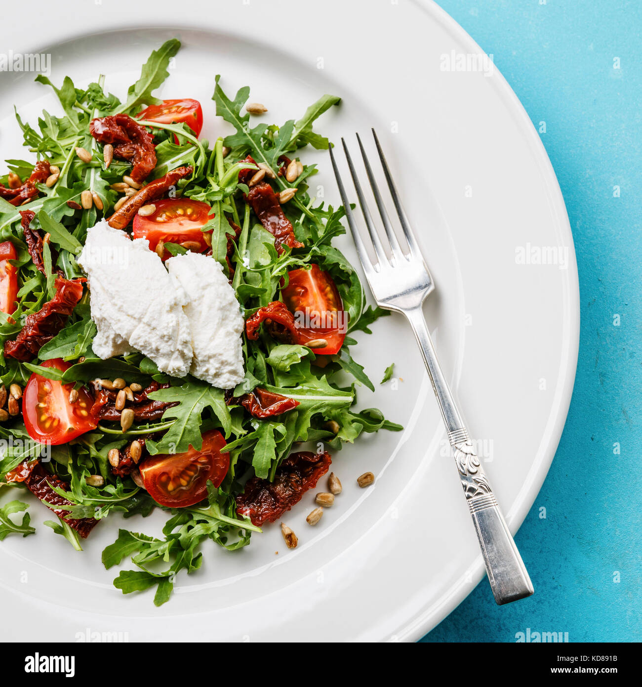 Avec salade de roquette, tomates séchées, les graines de tournesol et de ricotta sur plaque blanche close-up Banque D'Images