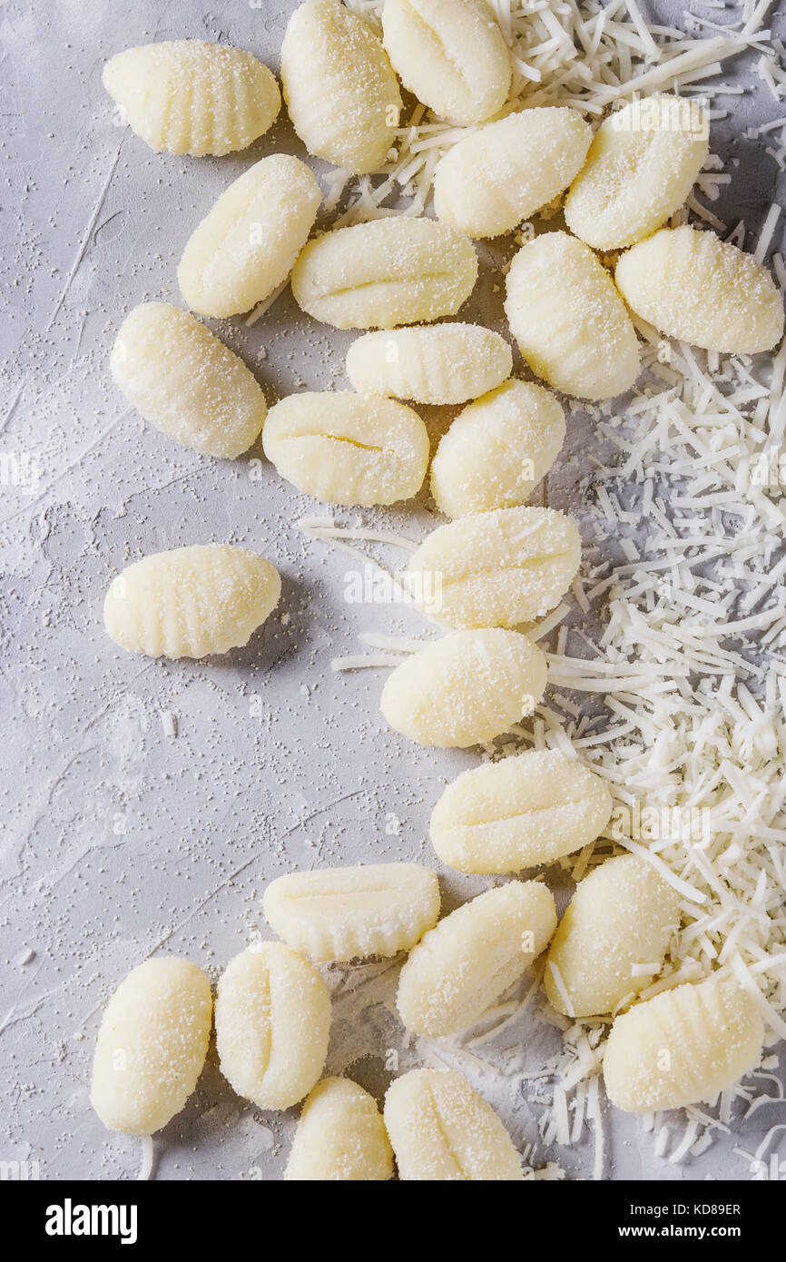 Gnocchi de pommes de terre non cuites brutes avec la farine et le parmesan râpé sur fond de béton gris. Vue de dessus, Close up. La cuisine maison. Banque D'Images