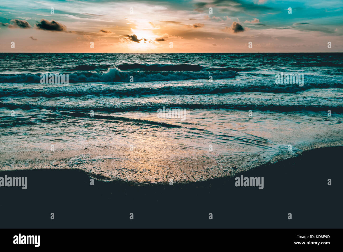 Lever de soleil brillant dans le ciel de couleur sable foncé et des vagues Banque D'Images