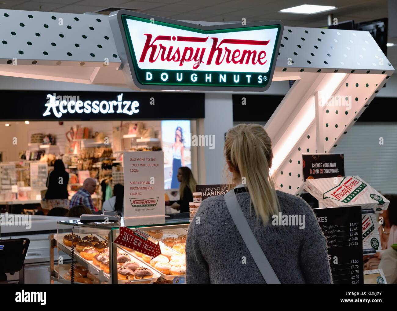 Une femme debout par un Krispy Kreme doughnut stand à l'aéroport international de Glasgow, Écosse, Royaume-Uni Banque D'Images