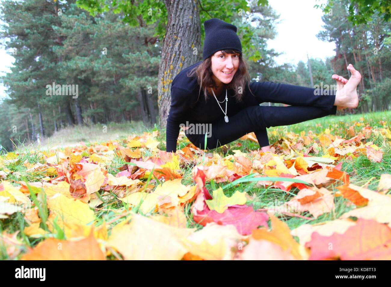 Belle femme souple fait la pratique du yoga sur l'herbe verte couverte de feuillage automne lumineux Banque D'Images