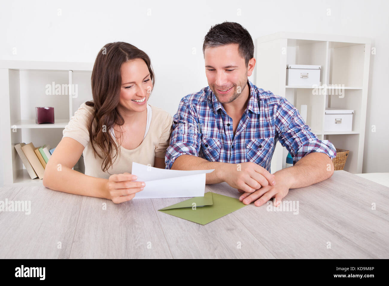 Portrait Of A Happy Young Couple At Home Reading Paper Banque D'Images