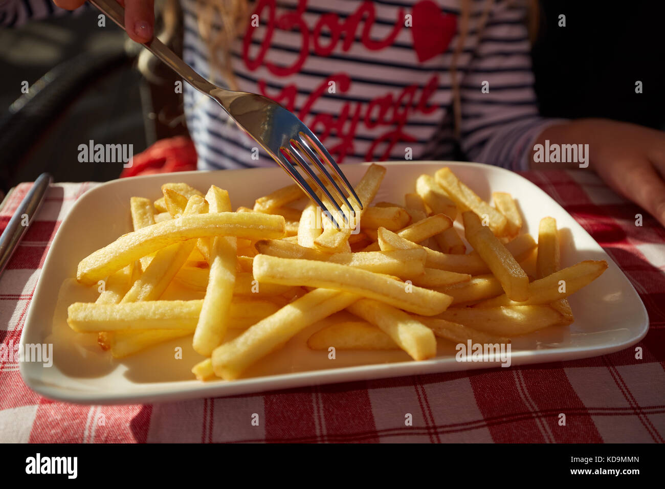 La photo en gros preschool girl mange des pommes de terre frites assis dans le café en plein air. Banque D'Images