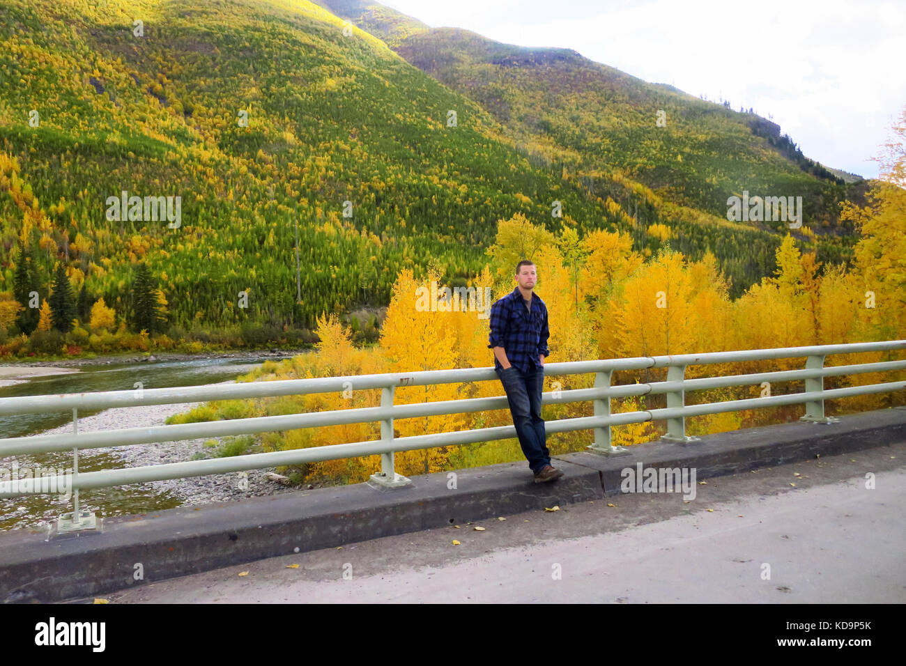 Un homme appuyé contre un pont avec une forêt et montagne derrière lui au Glacier National Park dans le Montana. Banque D'Images