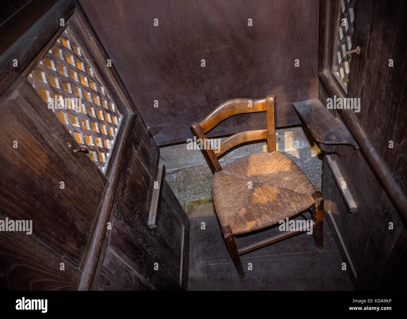 Église catholique confessionnelle cadre confessionnel rustique vue intérieure du petit fauteuil en osier du prêtre dans un simple confessionnel en bois dans une église catholique romaine Banque D'Images
