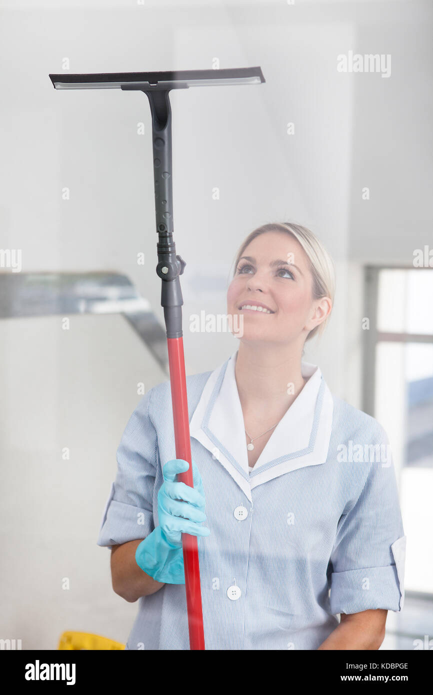 Happy woman nettoyage vitre avec vitres en caoutchouc Banque D'Images