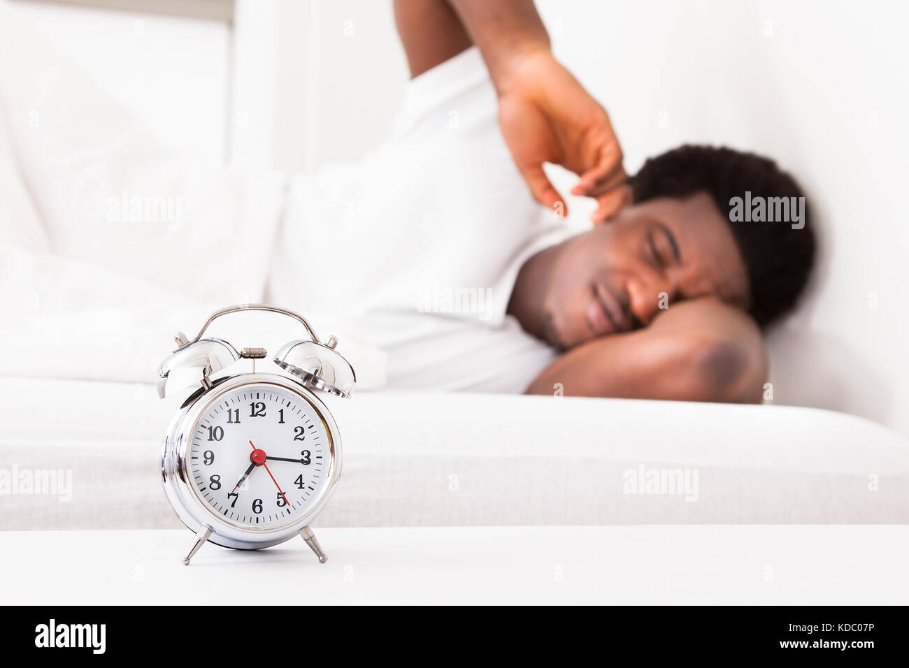 Homme frustré en essayant d'attraper est Réveil tout en vous relaxant sur  son lit Photo Stock - Alamy