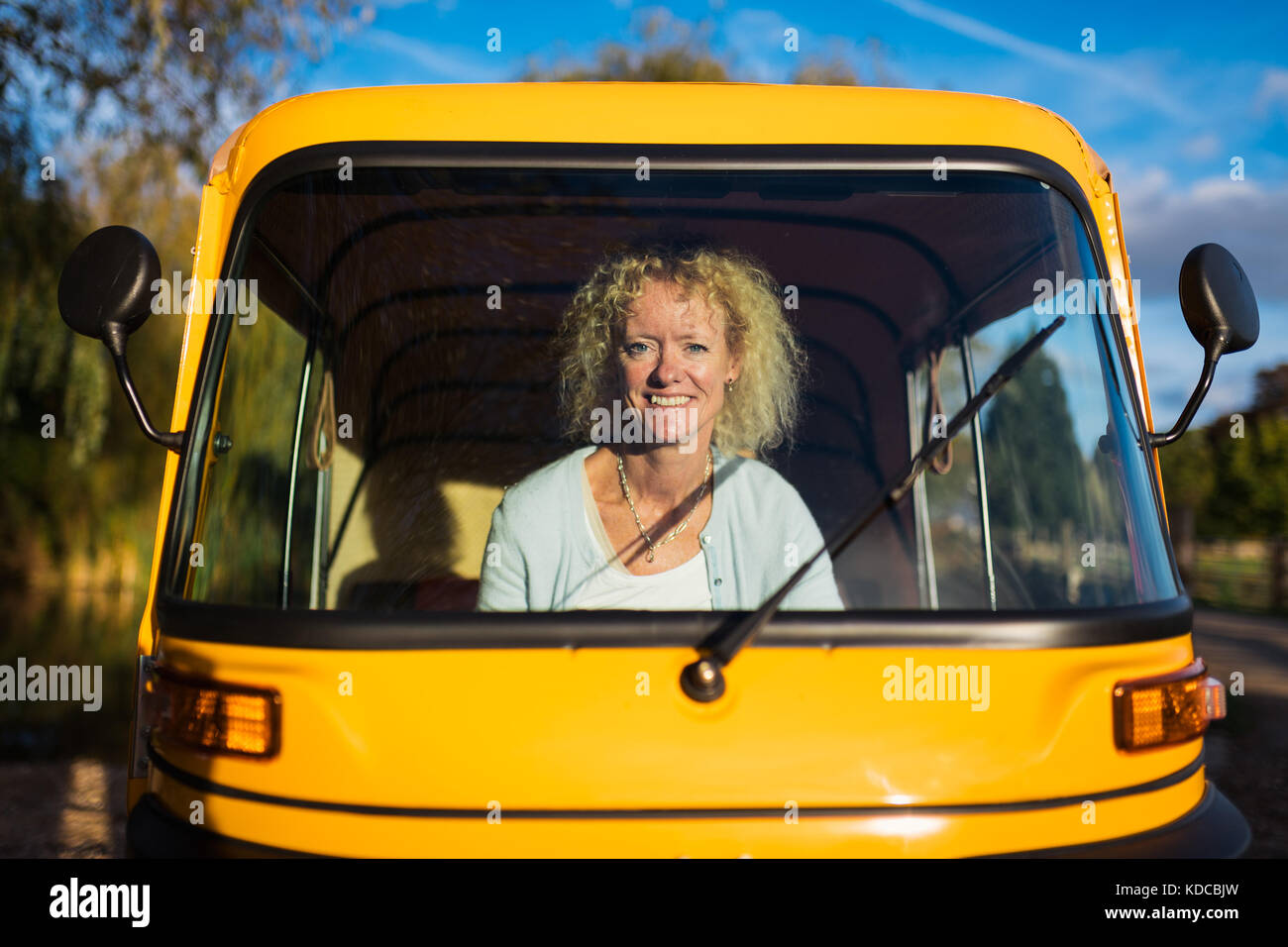 Une femme blonde conduit un tuk tuk jaune dans un village anglais Banque D'Images