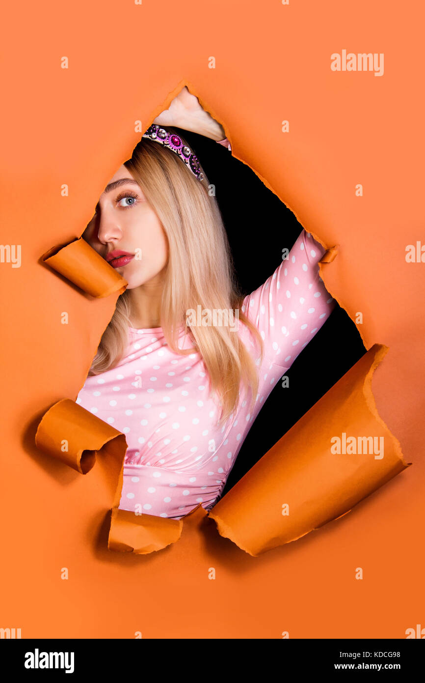 Jolie jeune femme regardant à travers un trou dans un papier orange Banque D'Images