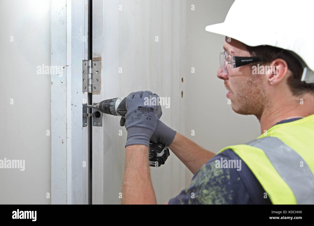 Un ouvrier installe un près dissimulé d'une nouvelle porte d'incendie dans le cadre de la rénovation d'un immeuble résidentiel à Londres, au Royaume-Uni. Banque D'Images