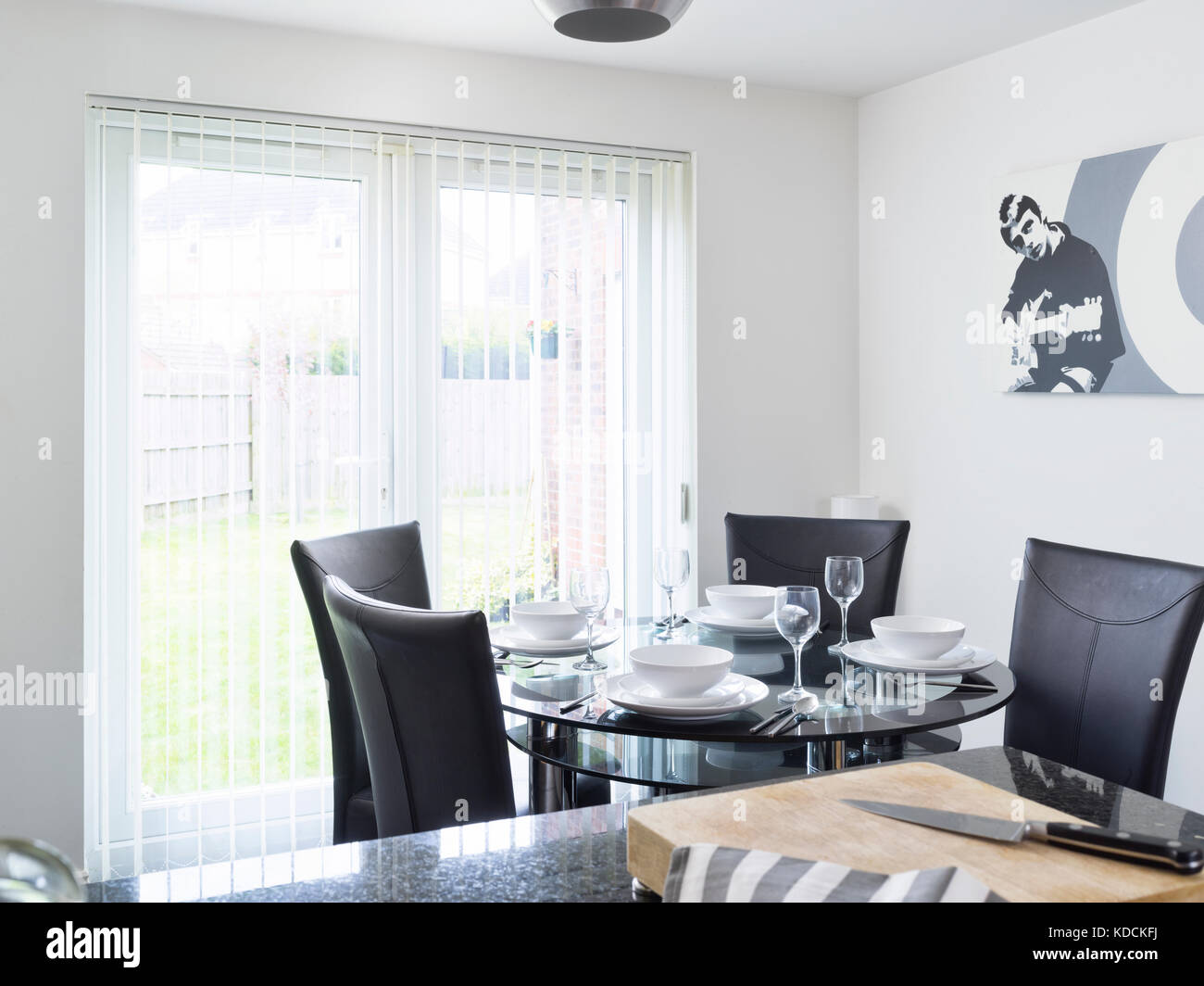 Un tour de table en verre avec chaises, habillé d'un repas dans une cuisine moderne conçu monochrome d'un contemporain de l'intérieur britannique. Banque D'Images