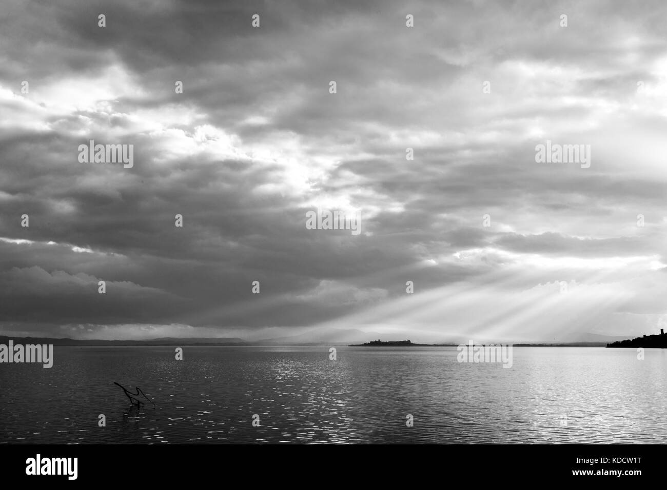 Les rayons du soleil émergeant dans les nuages au-dessus d'une île sur un lac, avec des branches au premier plan Banque D'Images