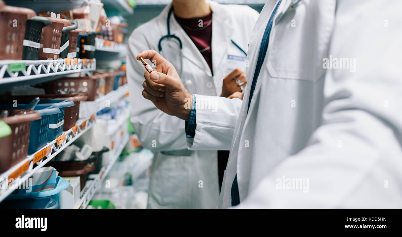 Deux pharmacien à la promotion de médicaments essentiels. Médecin homme tenant un médicament avec femme debout par en pharmacie. Banque D'Images